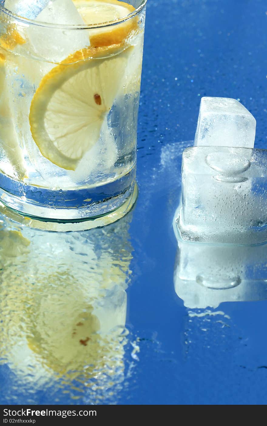 Glass of water with lemon and ice cubes on blue background. Glass of water with lemon and ice cubes on blue background