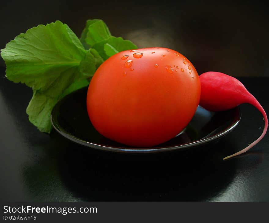 The Red Tomato With Radish On A Black Plate