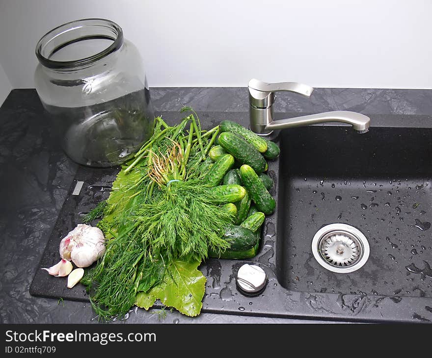 The big jar on the black sink with washed cucumbers and other ingredients ready to cucumbers pickling.