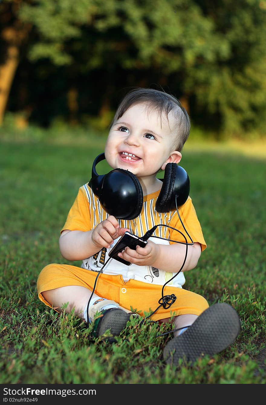 Little boy with headphones sitting on the grass. He was smiling from ear to ear. Little boy with headphones sitting on the grass. He was smiling from ear to ear