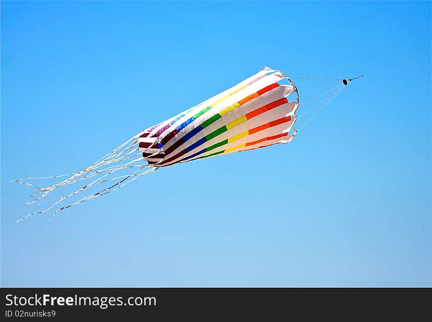 Colorful striped kite with streamers flying against the clear blue sky. Colorful striped kite with streamers flying against the clear blue sky.