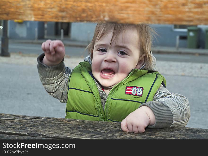 Angry little child behind the bench threatens. Angry little child behind the bench threatens