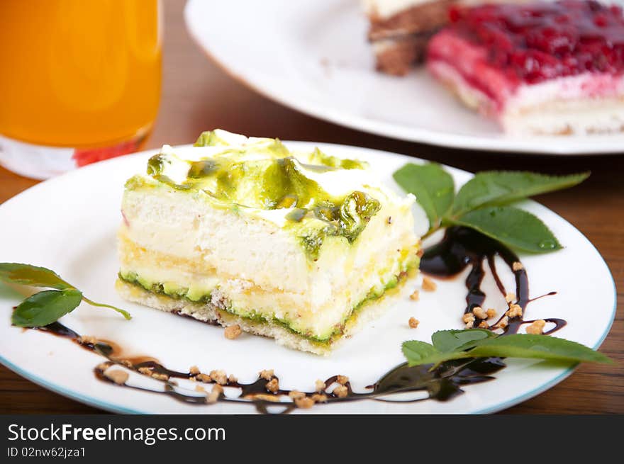 Sweet pistachio dessert with vanilla cream and nuts and chocolate on white plate with juice.