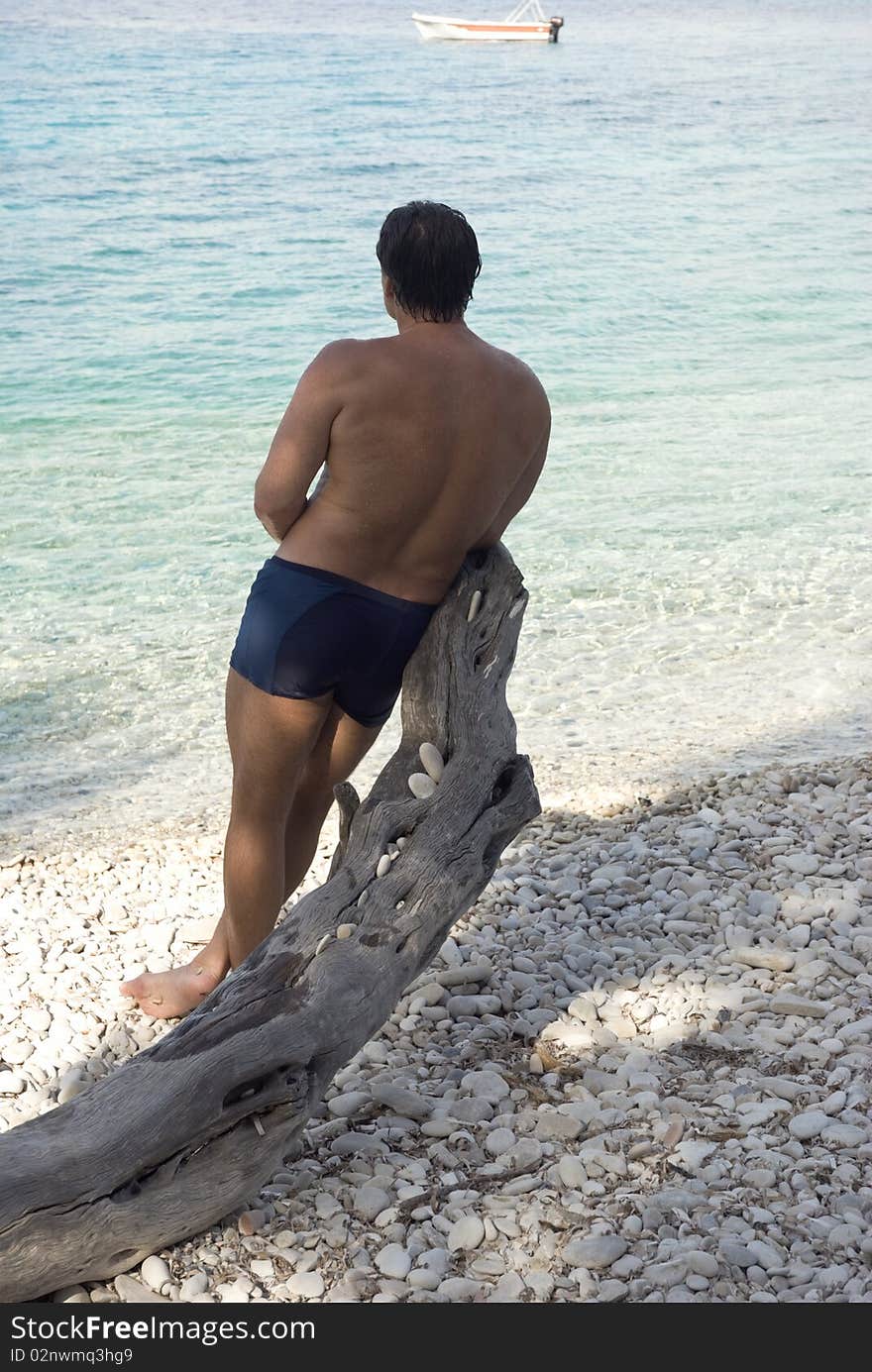 Man leang on tree on a pebbly beach in Paxos Greece