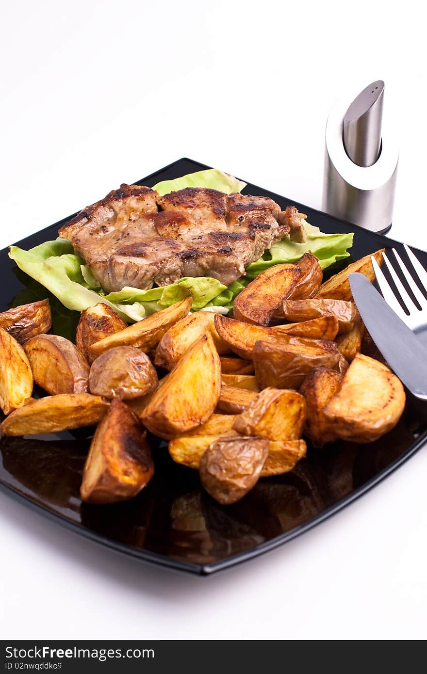 Pork and fried potatos on black plate. Pork and fried potatos on black plate