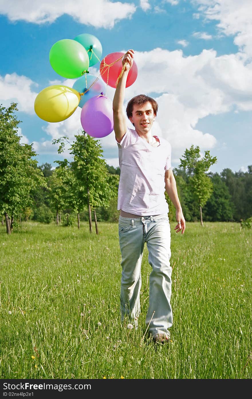 Young man with many colored balloons at green summer lawn