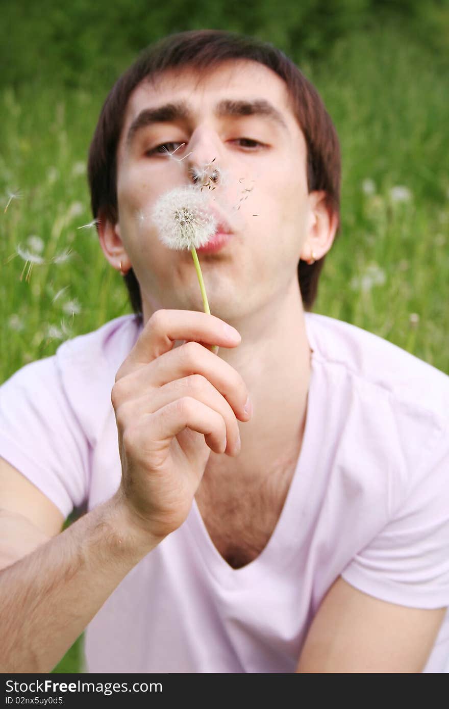 Young man blowing at dandelion focus on flower