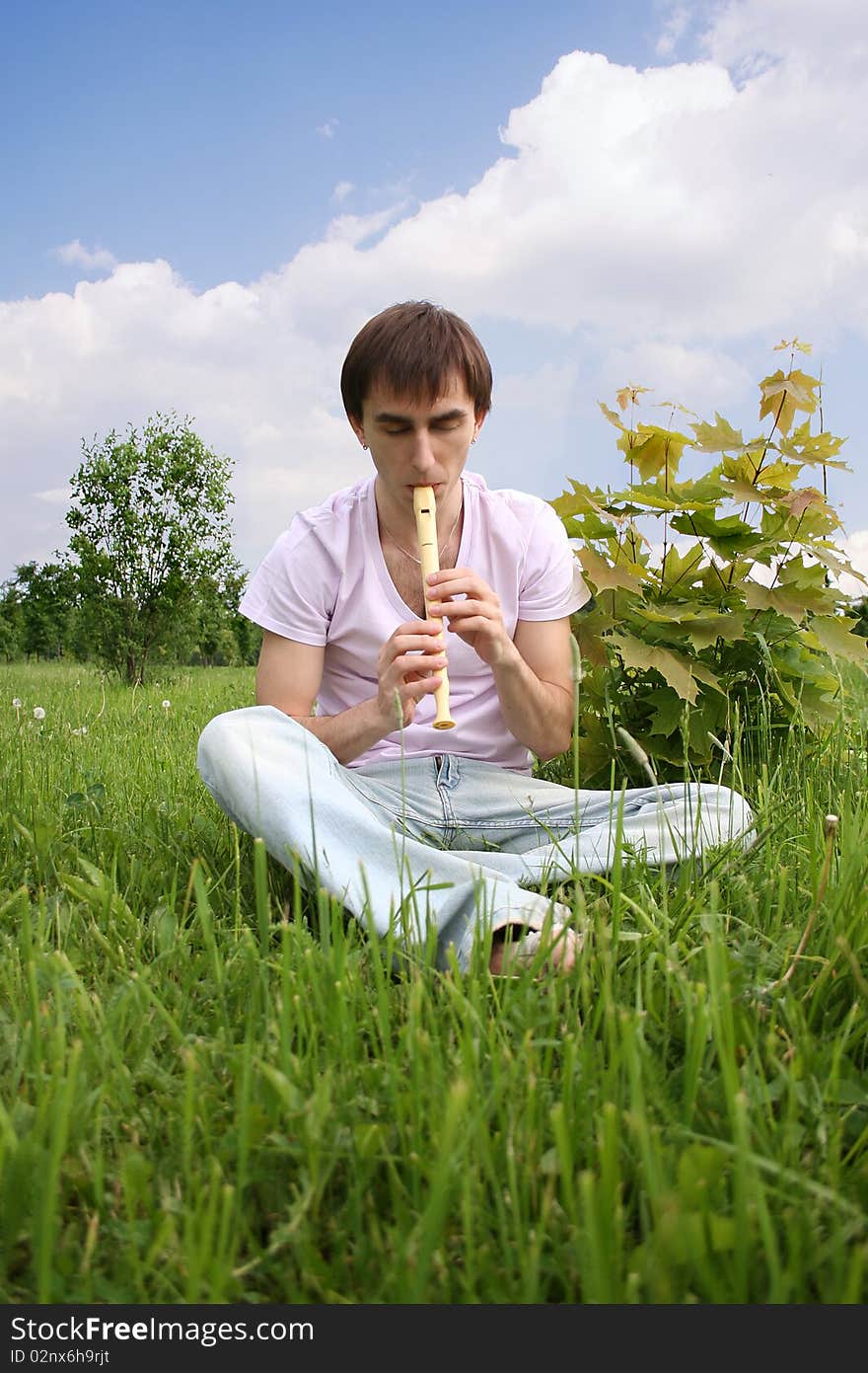 Young man playing on flute at summer time outdoor