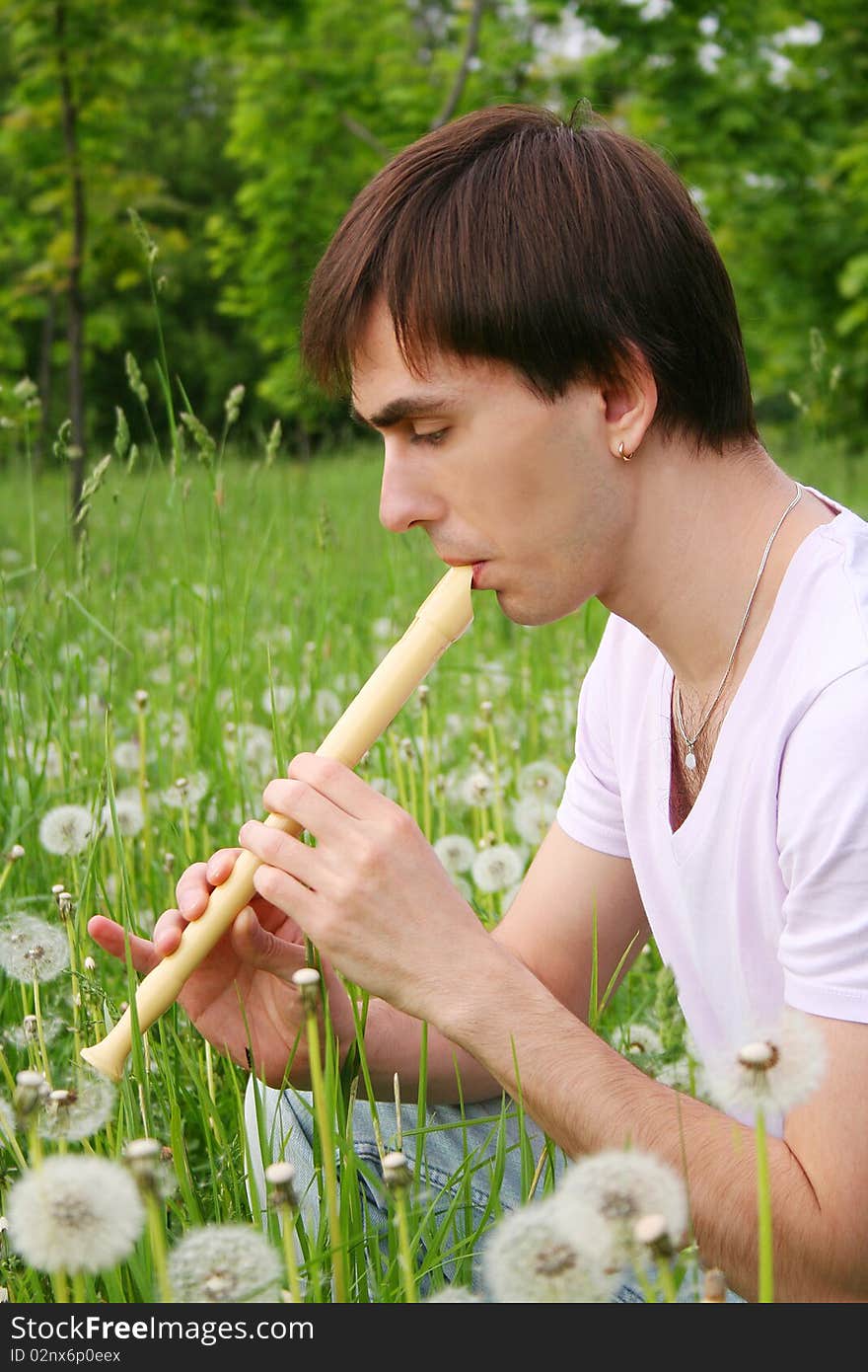 Young man playing on flute at summer time outdoor side view. Young man playing on flute at summer time outdoor side view