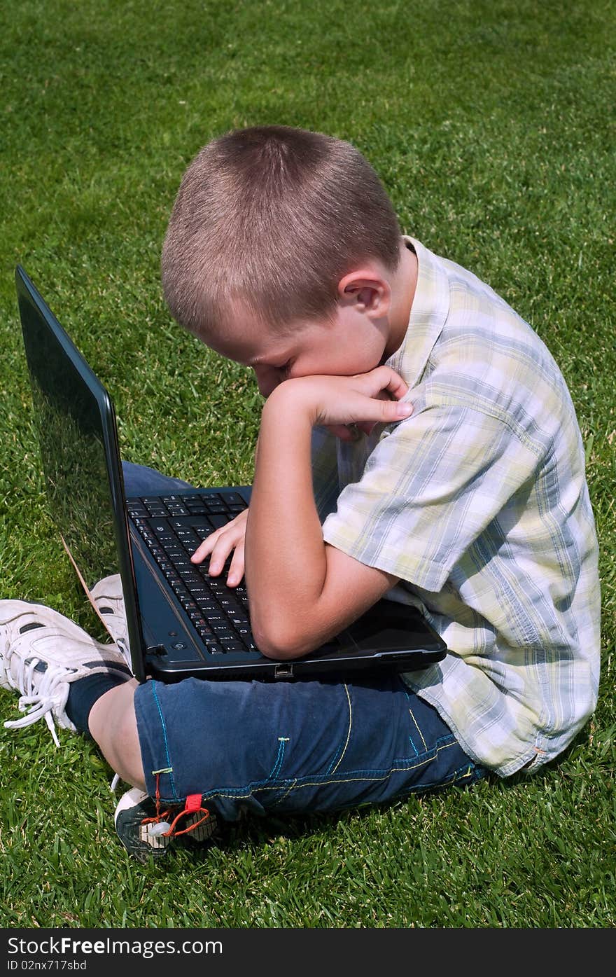 Boy playing with laptop outdoors on green grass