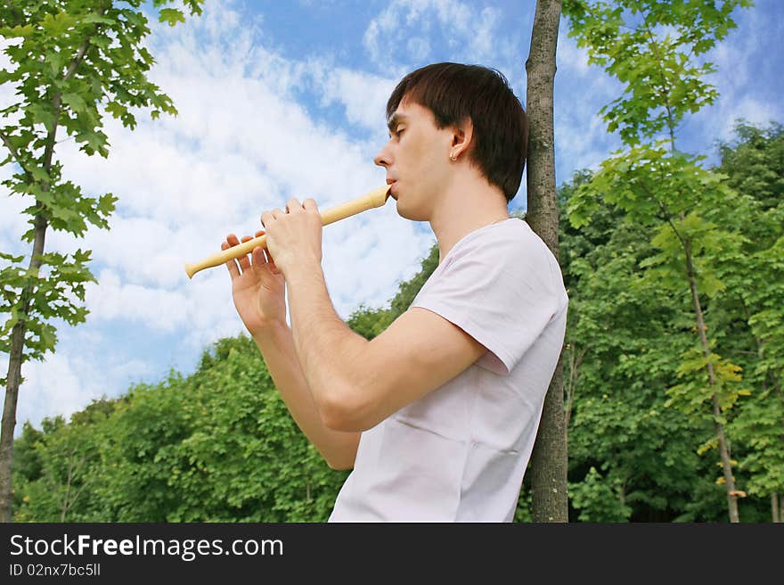 Young man playing on flute at summer time outdoor side view