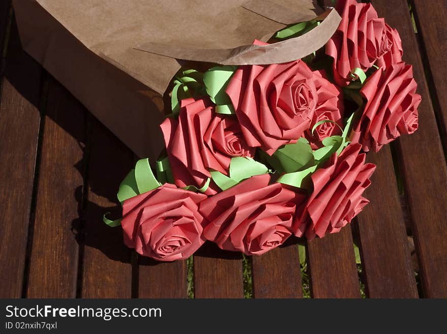 Red paper roses in a brown paper bag on a garden table