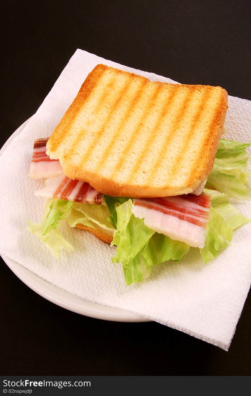 The toast with bacon, cheese and salad is prepared on a black background