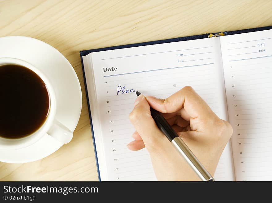 On the table is a laptop and a cup of coffee. Women's Hand wrote the text of the plan. On the table is a laptop and a cup of coffee. Women's Hand wrote the text of the plan