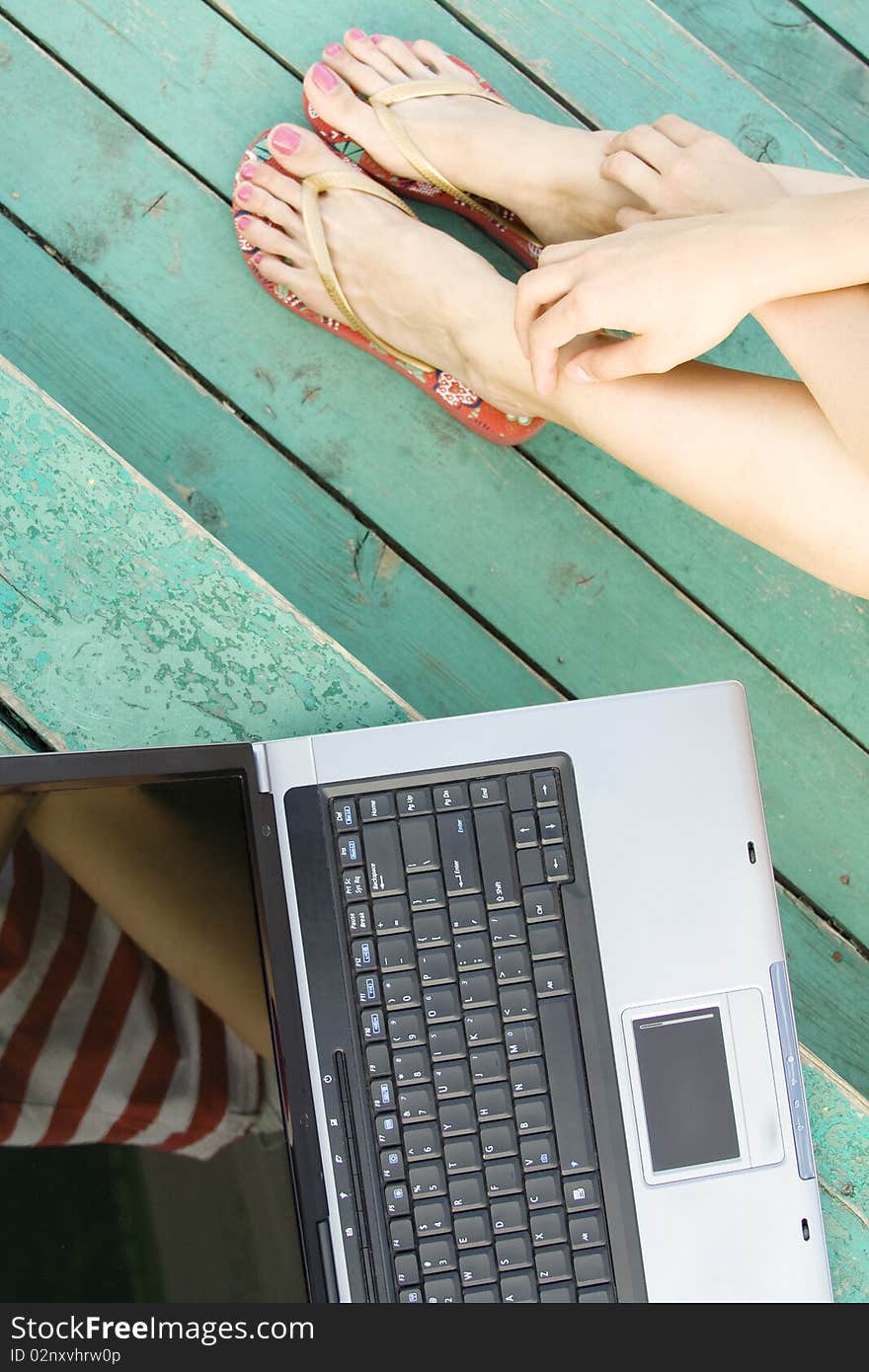 Women's hands and feet next to the laptop on a wooden staircase. Top view. Women's hands and feet next to the laptop on a wooden staircase. Top view