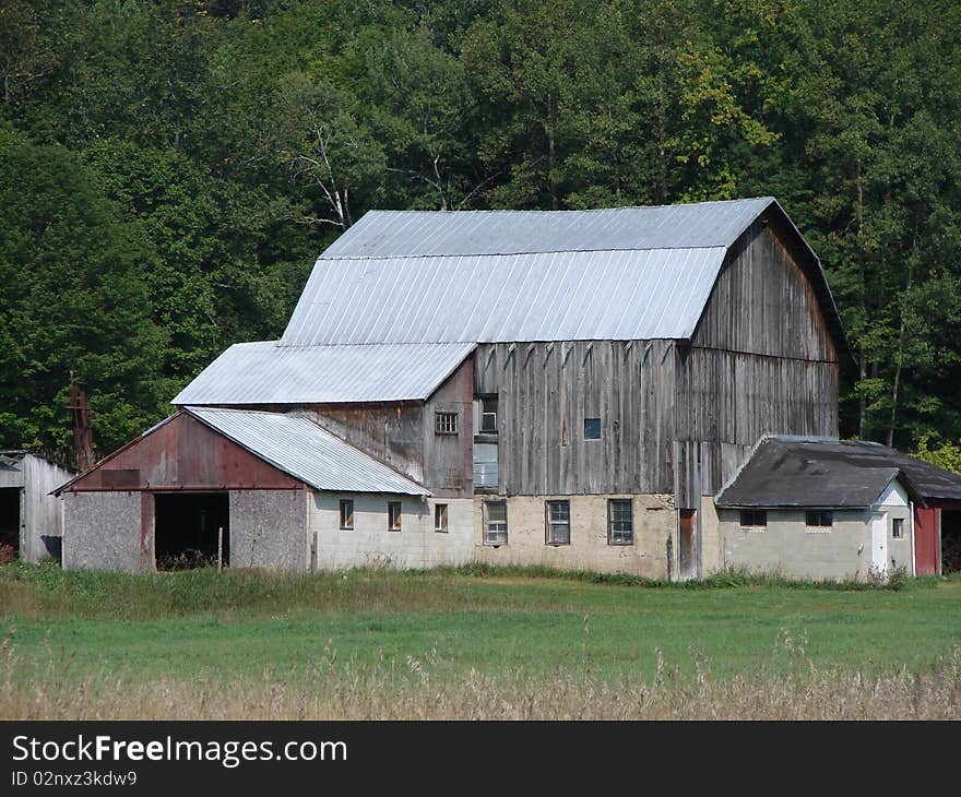 Old wood and metal barn in field with trees Barn has many additions to it. Old wood and metal barn in field with trees Barn has many additions to it.