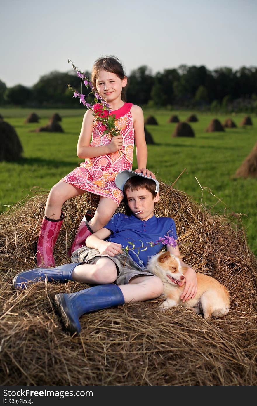 Summer lanscape with hay cocks, couple children sitting on large hay