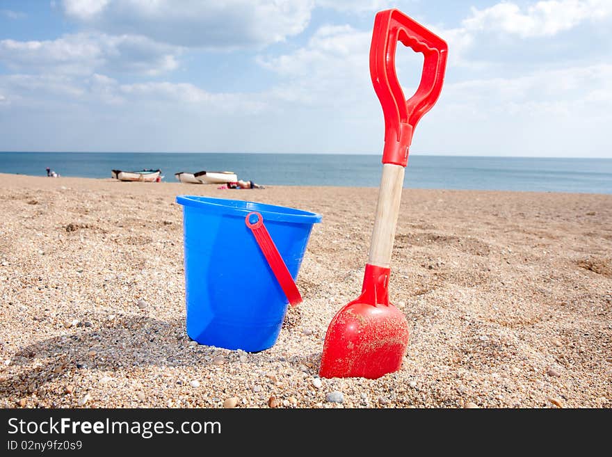 A blue bucket and a red spade on a sandy beach on a sunny afternoon. A blue bucket and a red spade on a sandy beach on a sunny afternoon.