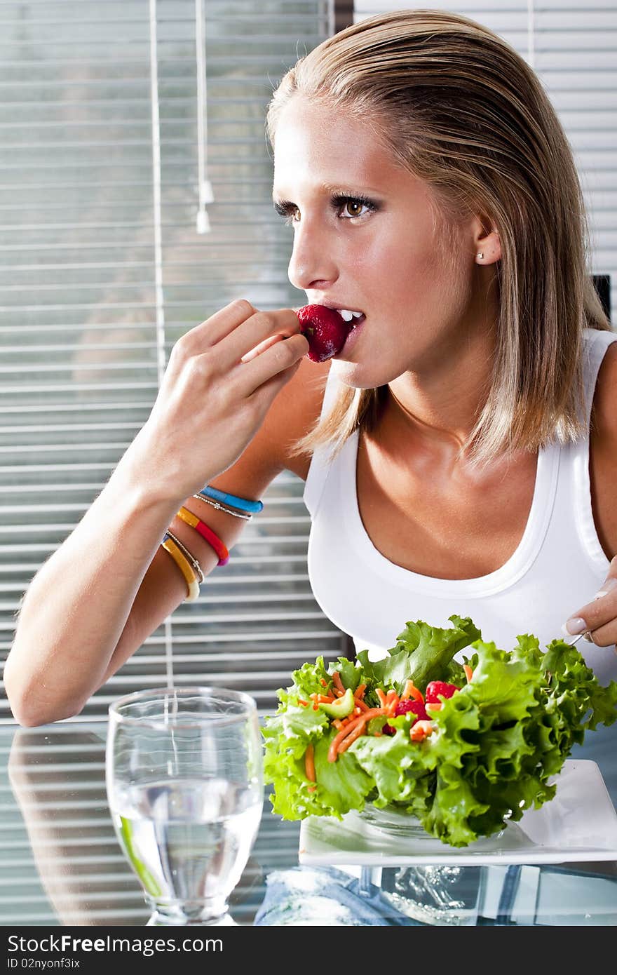 Young women at home biting on a strawberry eating a salad. Young women at home biting on a strawberry eating a salad