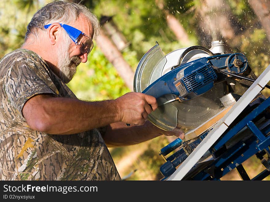 Senior man in protective goggles cutting wood with a chop saw. Senior man in protective goggles cutting wood with a chop saw.