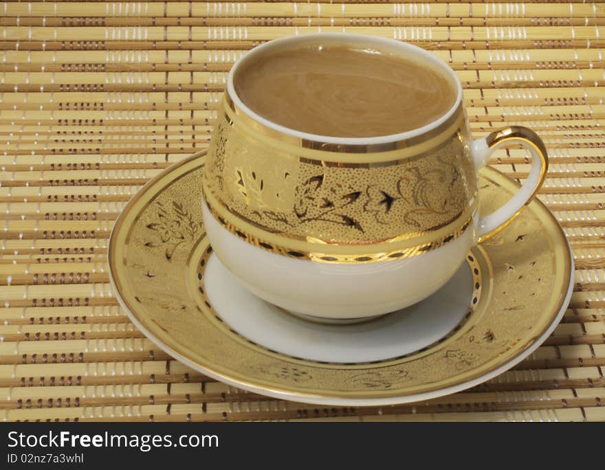 Coffee with milk in a cup with a gold pattern, cup and saucer on a bamboo cloth, the color of ocher