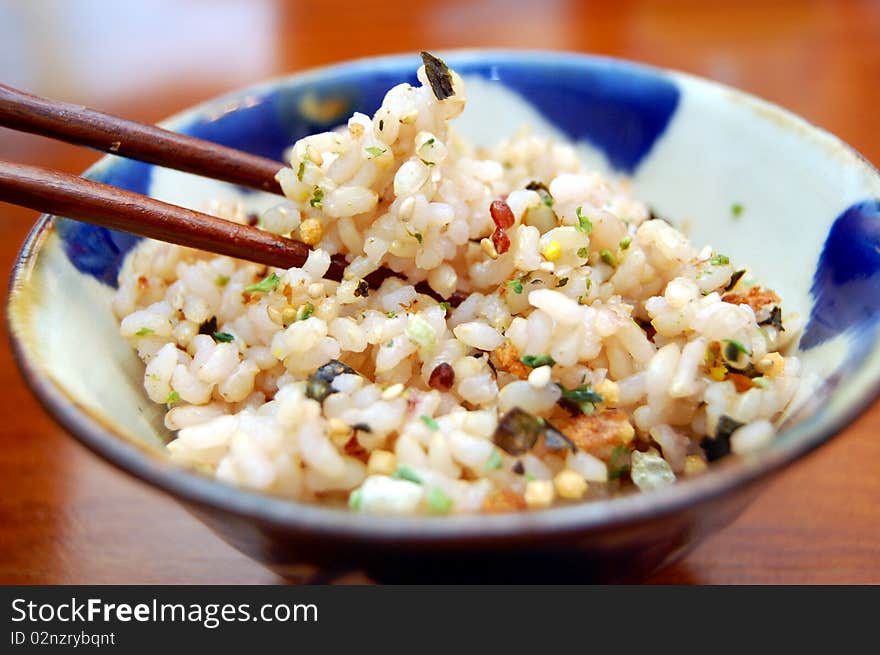 A rice bowl with seasoning and chopsticks holding up rice.