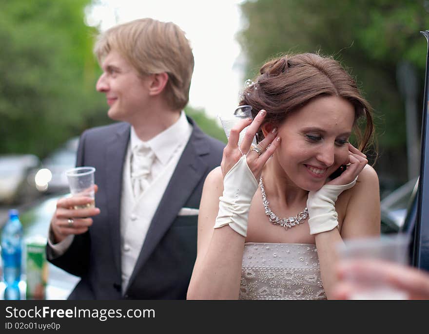 Young bride getting wedding greetings by cell phone. Groom is nearby.