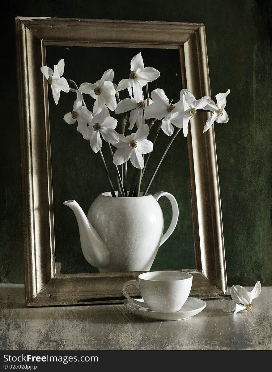 the bouquet of narcissuses is costed in a tea-pot, next to them cup. the bouquet of narcissuses is costed in a tea-pot, next to them cup