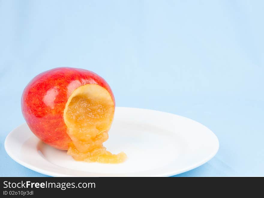 Cinnamon apple sauce spilled from cored apple on white plate