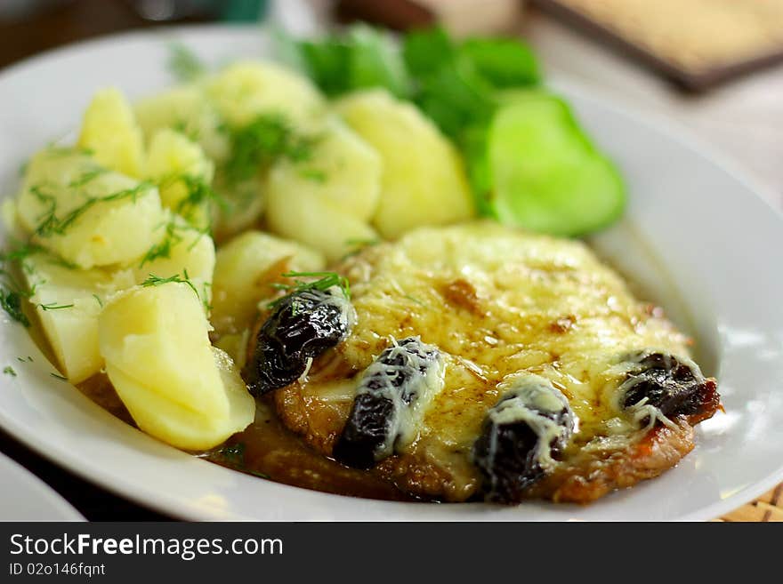 Dish with a pork chop and potatoes with dried plums, cheese and culinary plants. Dish with a pork chop and potatoes with dried plums, cheese and culinary plants.