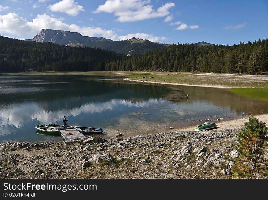 View of Black lake in Durmitor National park with stony coast, boats and fishermen, Montenegro. View of Black lake in Durmitor National park with stony coast, boats and fishermen, Montenegro