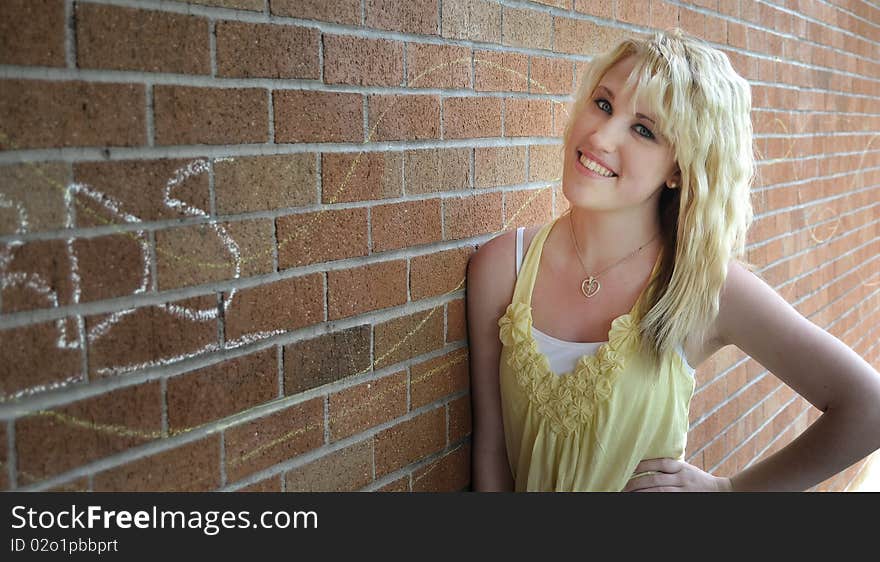 Happy young blond teenage girl standing in front of a brick wall smiling. Happy young blond teenage girl standing in front of a brick wall smiling.