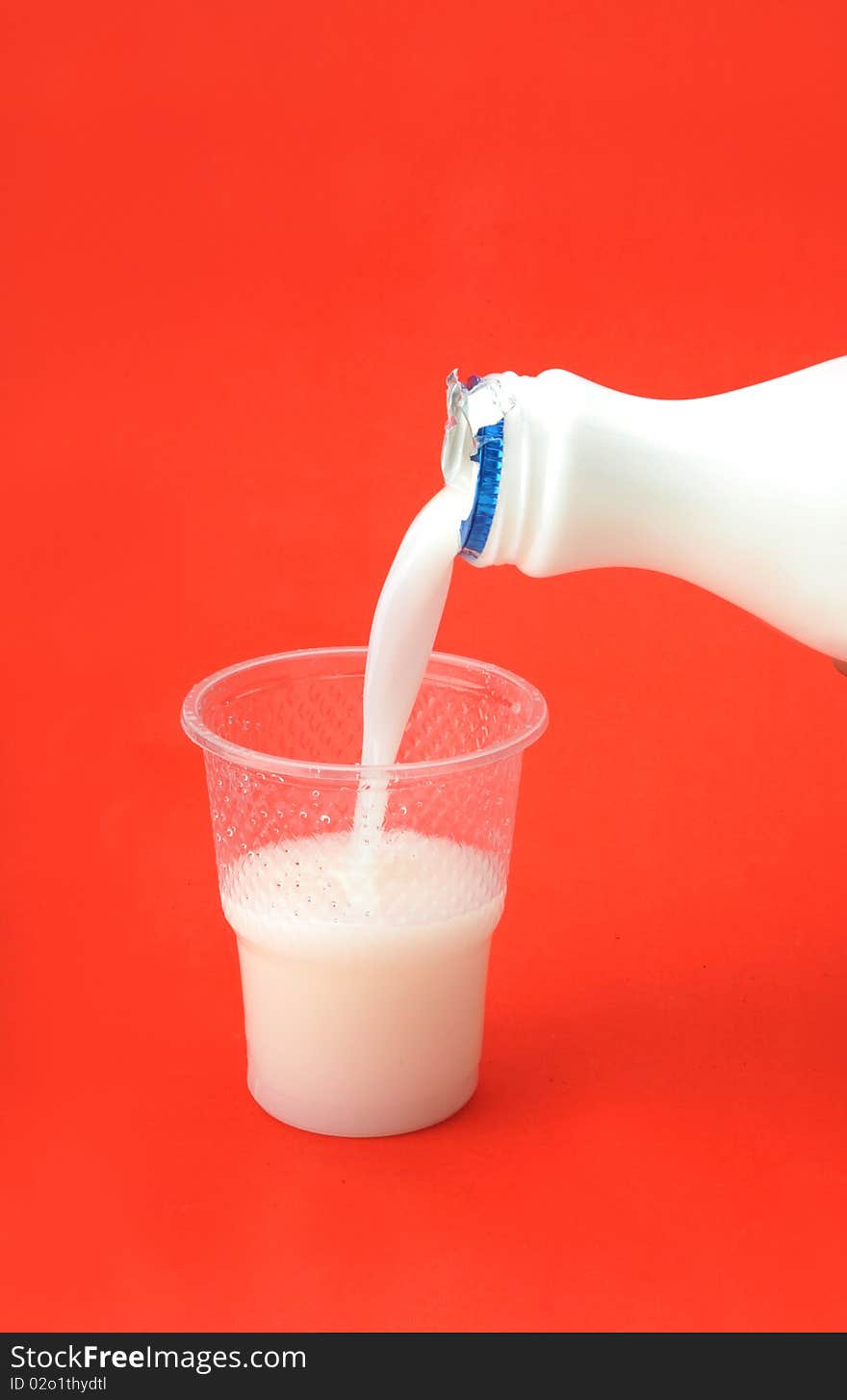 Milk inflow plastic cup over red background