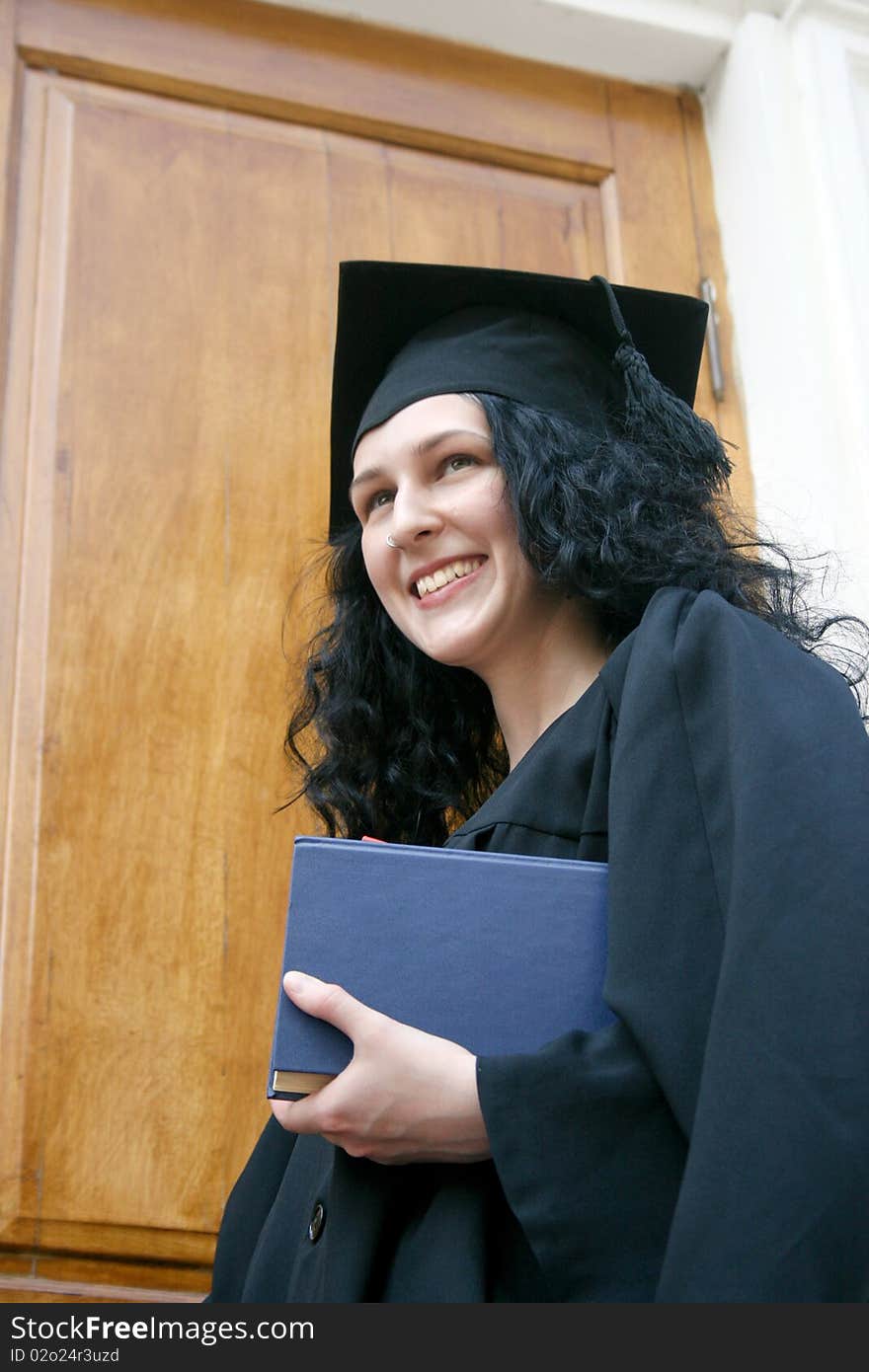 Young laughing student in gown near the university