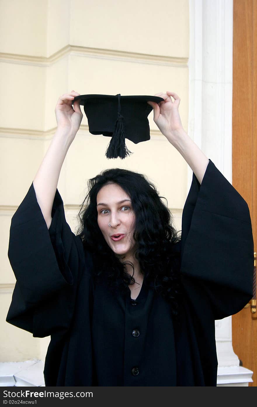 Young student in gown near the university trying on the cap. Young student in gown near the university trying on the cap