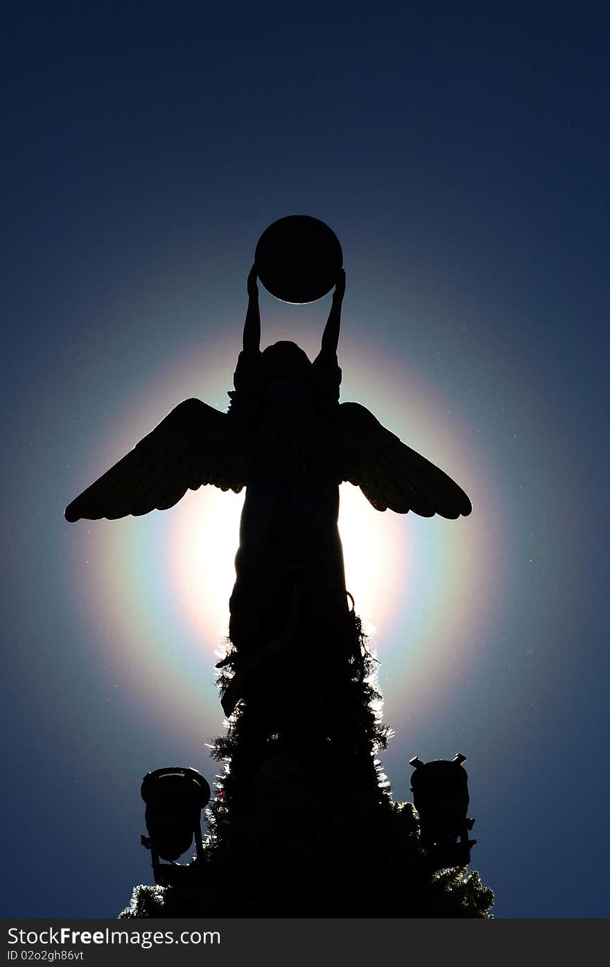 Silhouette of an angel tree topper on top of a huge Christmas tree. Silhouette of an angel tree topper on top of a huge Christmas tree