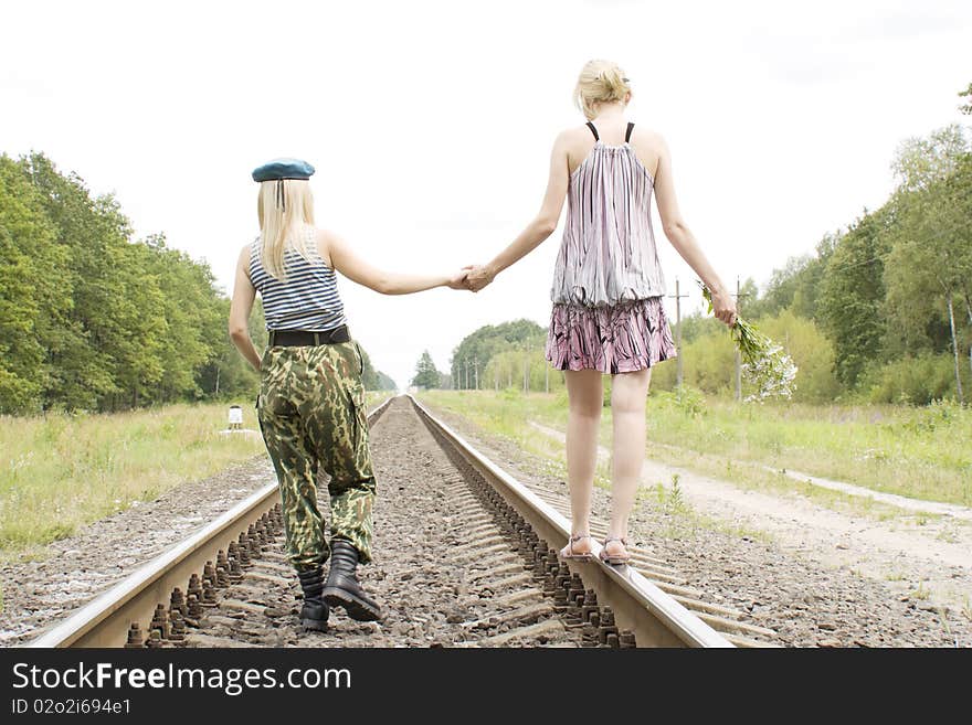 The woman in the military form goes on rails and holds a hand of the woman in a dress with a bouquet. The woman in the military form goes on rails and holds a hand of the woman in a dress with a bouquet