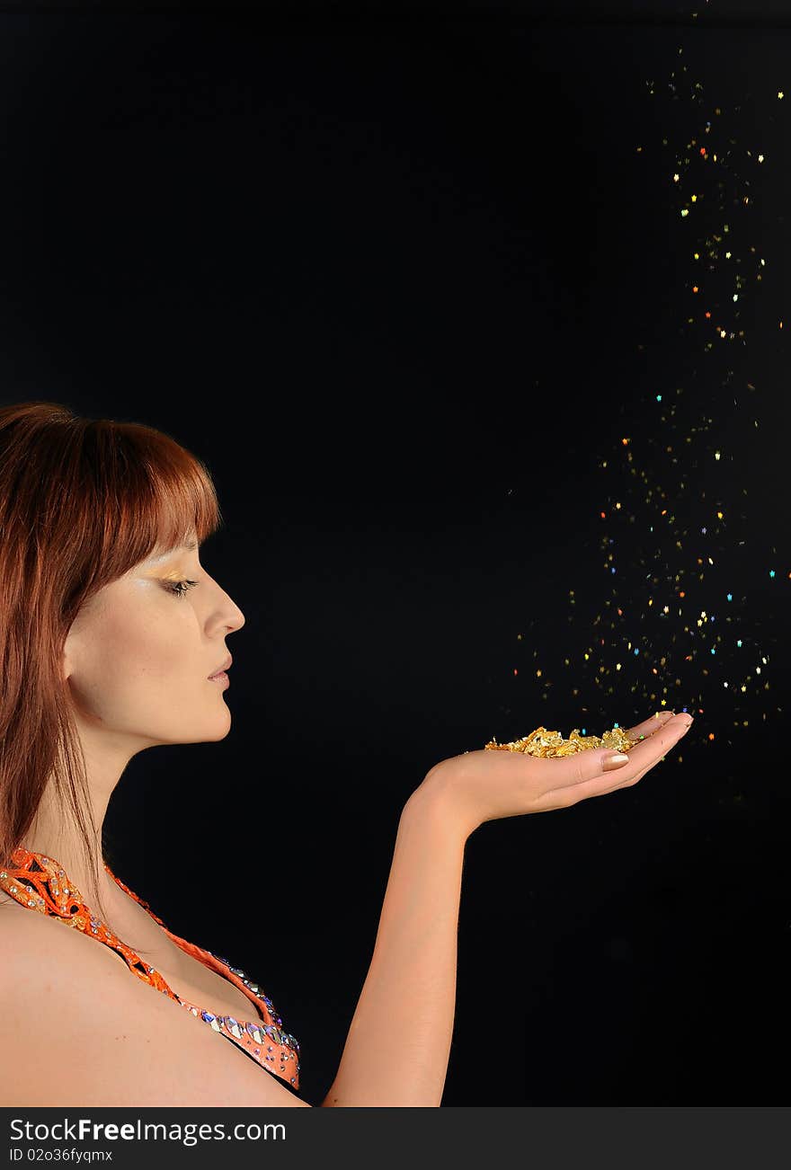 Young beautiful woman blowing golden stardust from her hand