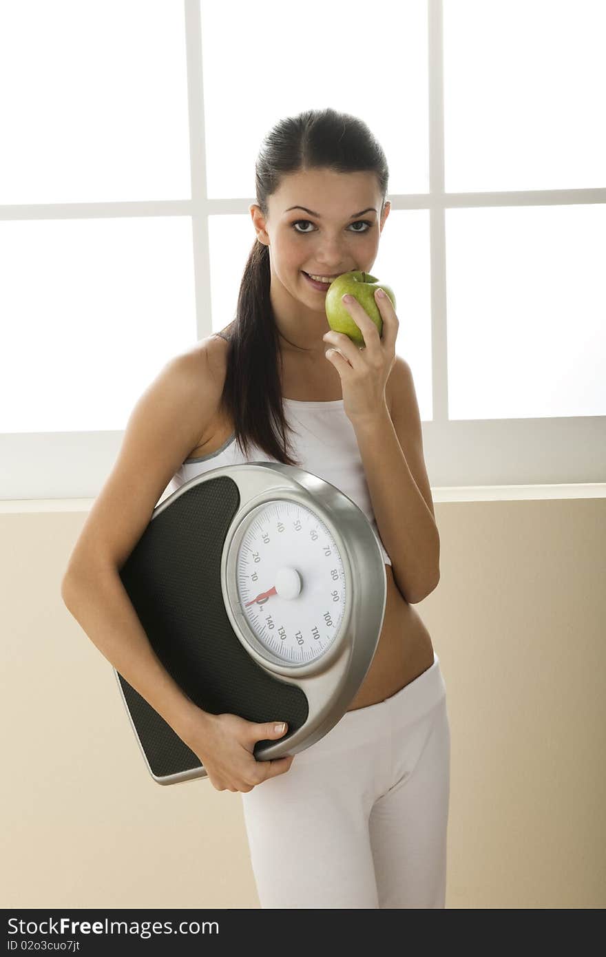 Young woman holding weight scale and eating apple