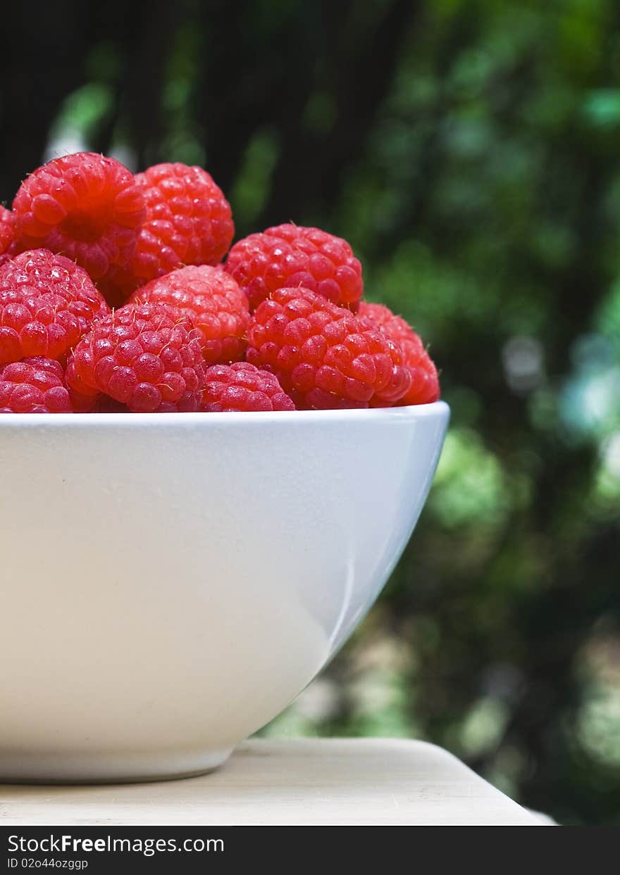 A white bowl of ripe strawberries on a cutting board on green background