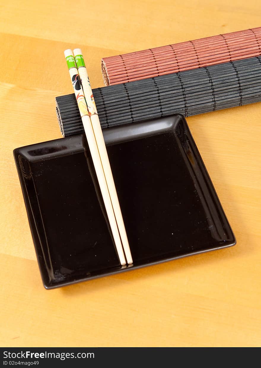 Two rolled bamboo mats with a square black plate and chopsticks. Two rolled bamboo mats with a square black plate and chopsticks