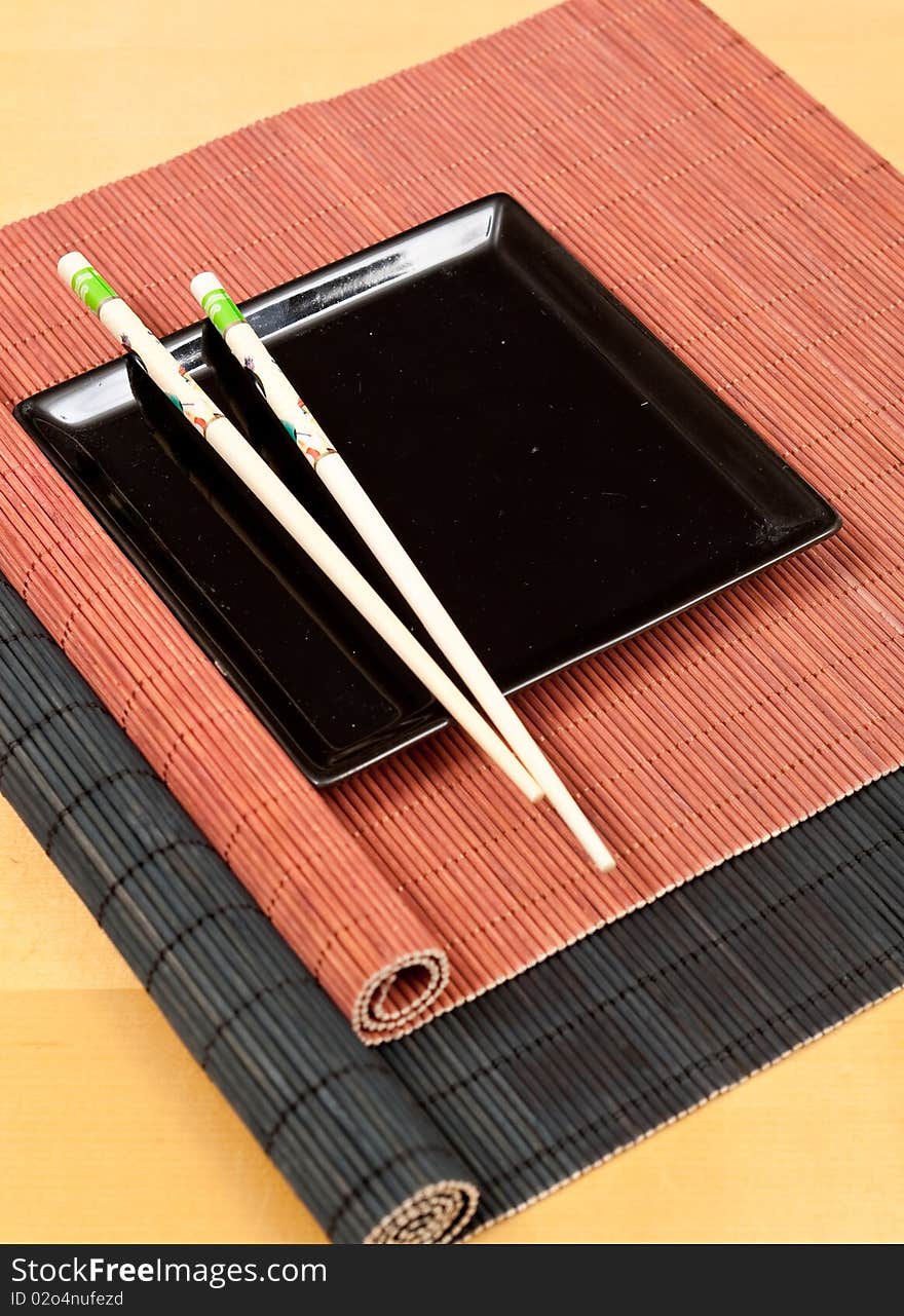 Oriental dining concept through black square plate and chopsticks on bamboo place mats. Oriental dining concept through black square plate and chopsticks on bamboo place mats