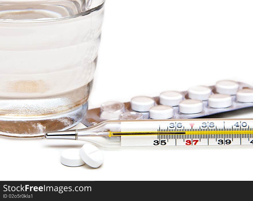 Glass with water, tablets, the medical thermometer on a white background. Glass with water, tablets, the medical thermometer on a white background