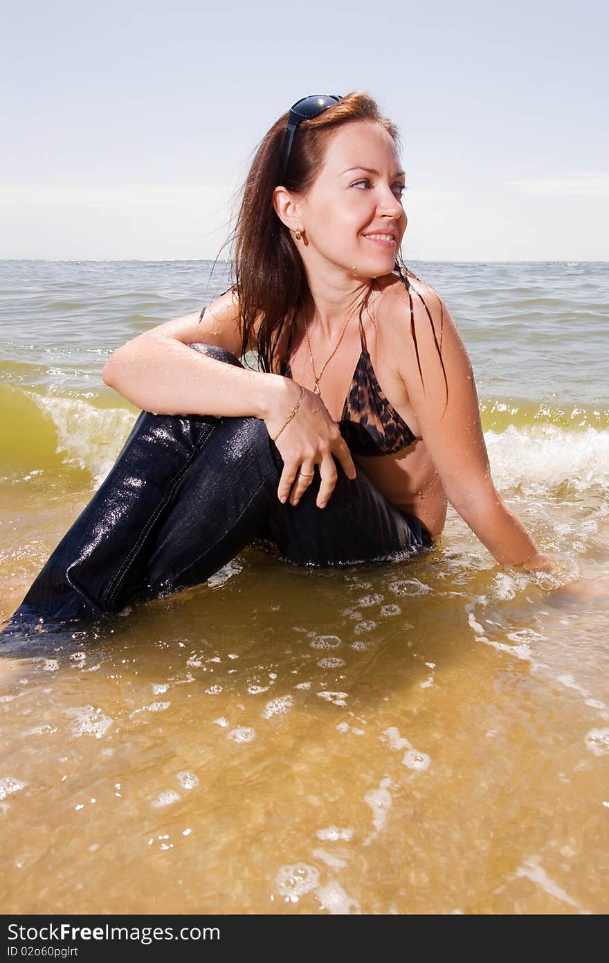 Young adult woman in wet jeans sits in splashes of tidal waves of a sea smiling. Young adult woman in wet jeans sits in splashes of tidal waves of a sea smiling