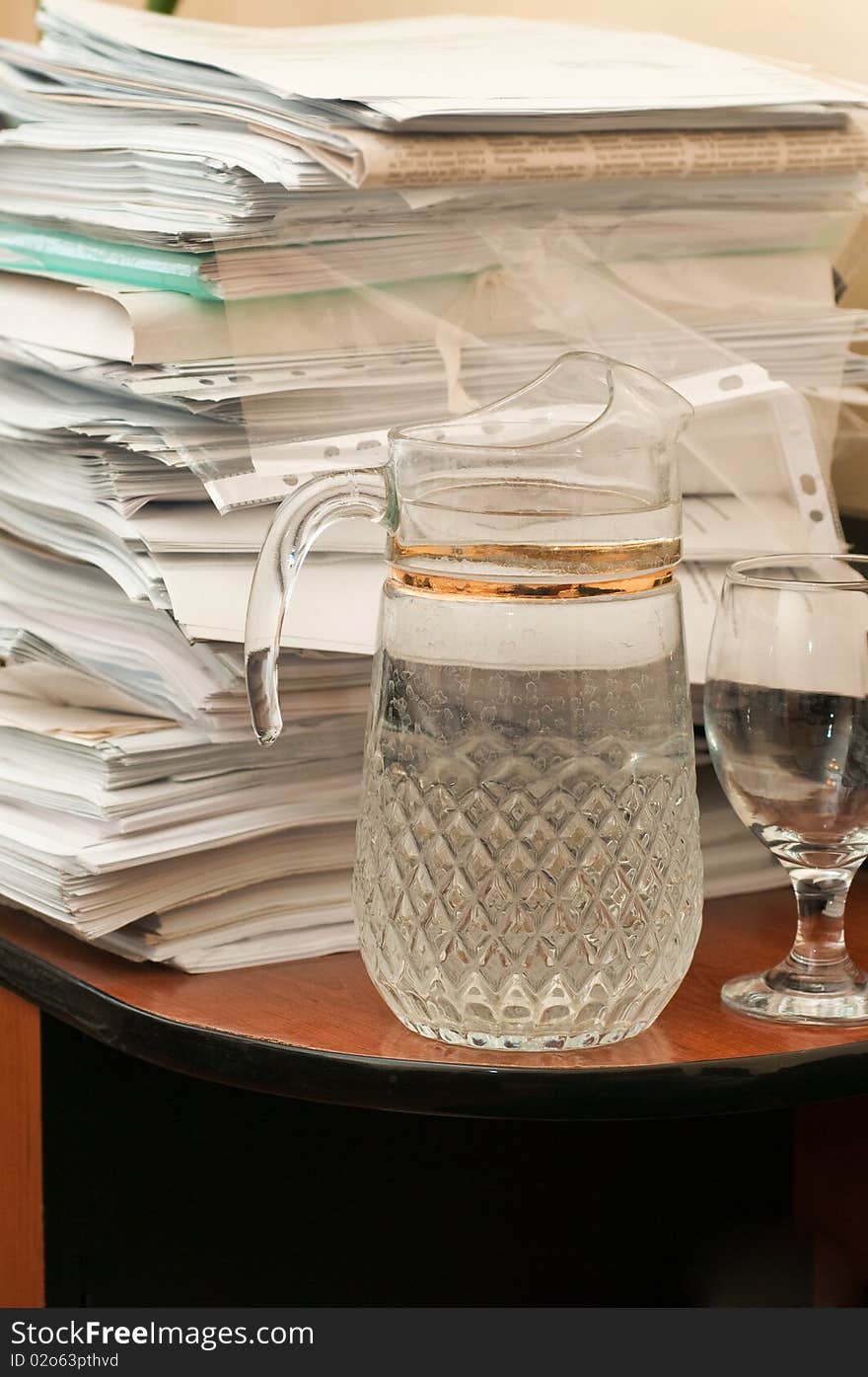 The big foot of various papers on a table at office and a decanter with potable water. The big foot of various papers on a table at office and a decanter with potable water.