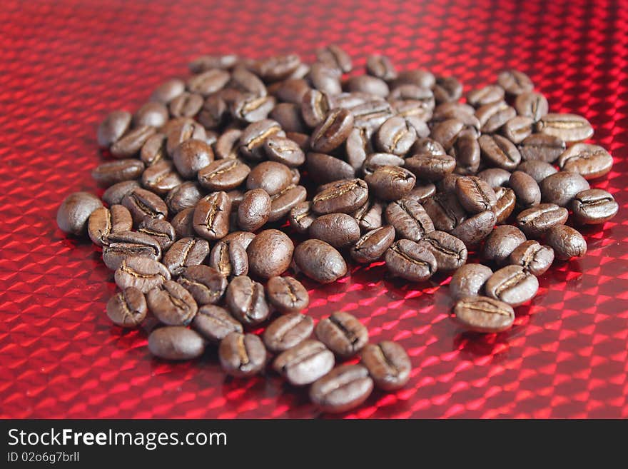 Roasted whole coffee beans scattered across a reflective red background. Roasted whole coffee beans scattered across a reflective red background