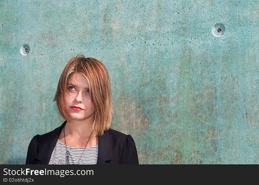 Attractive blonde girl thinking by concrete wall. Attractive blonde girl thinking by concrete wall