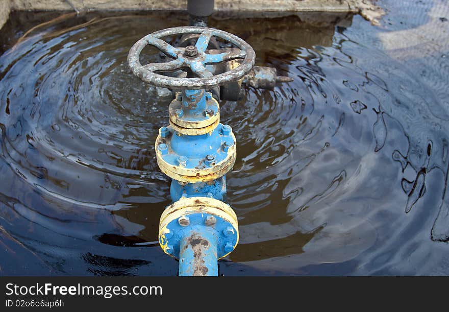 Barrel of oil over a blue tank with oil valve. Barrel of oil over a blue tank with oil valve