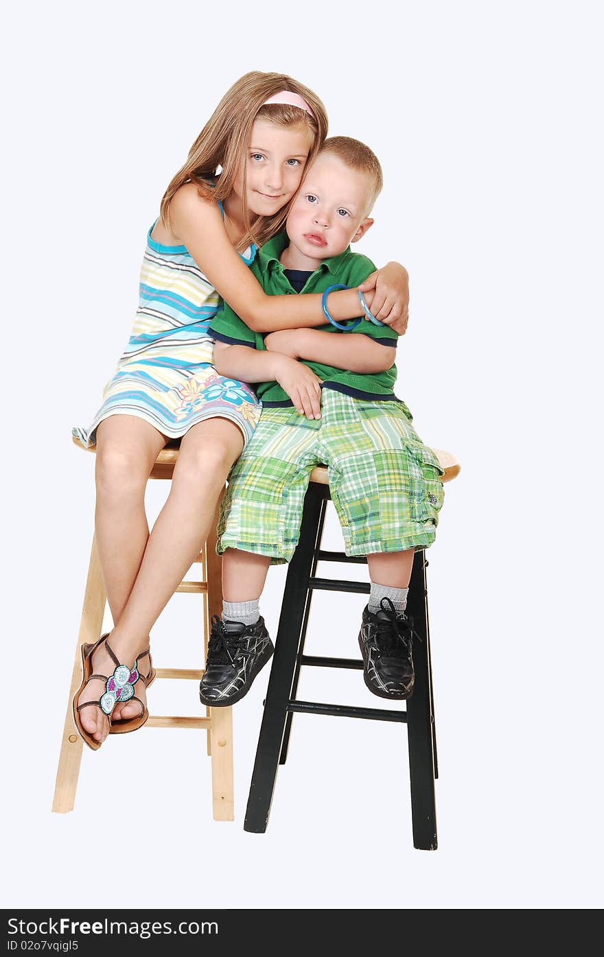 An pretty girl sitting with her brother on chairs and giving him a big hug on light blue background. An pretty girl sitting with her brother on chairs and giving him a big hug on light blue background.