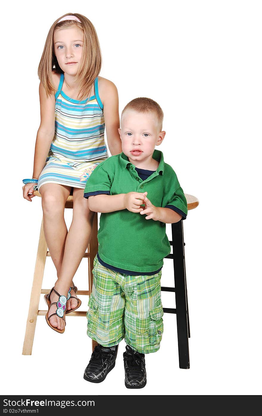 An seven year old girl sitting on a chair and her little brother standing in front of his chair in a green outfit for white background. An seven year old girl sitting on a chair and her little brother standing in front of his chair in a green outfit for white background.